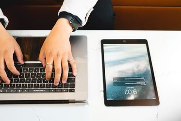 hands type on a laptop that is next to a tablet