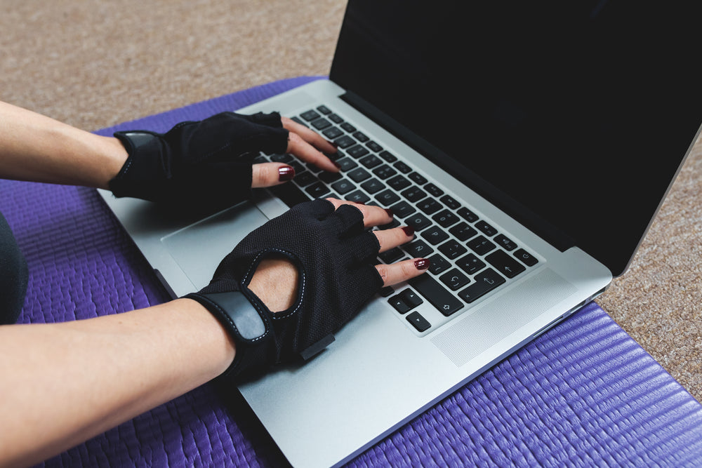 hands wearing black workout gloves type on laptop