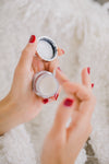 hands with red nails hold a small cosmetics container