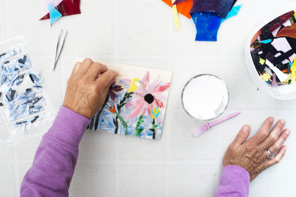 hands working on a floral mosaic on a grey table