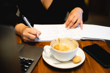 hands write in a open notebook next to an empty coffee cup