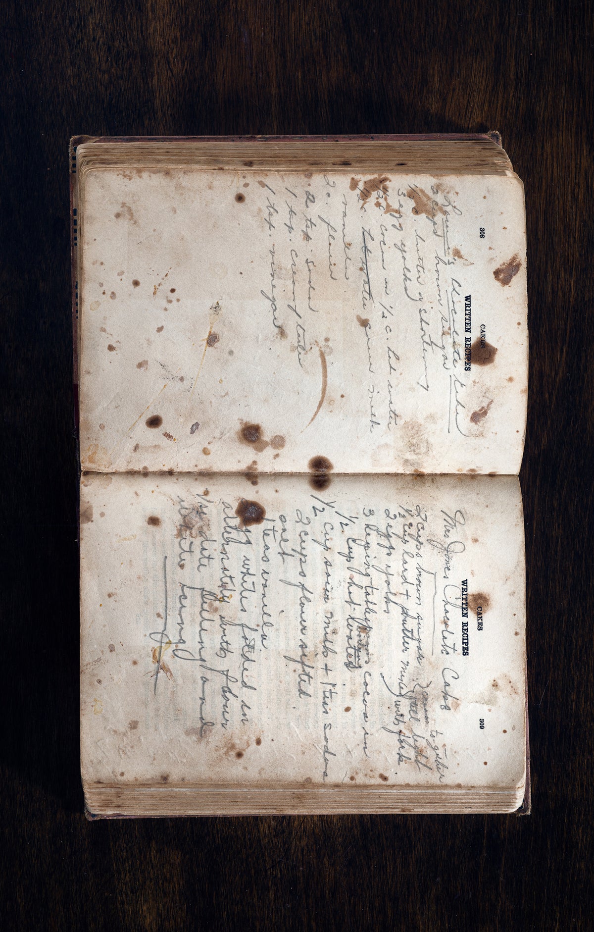 Handwritten Cookbook Lays Open To The Cake Section In A Wooden Surface