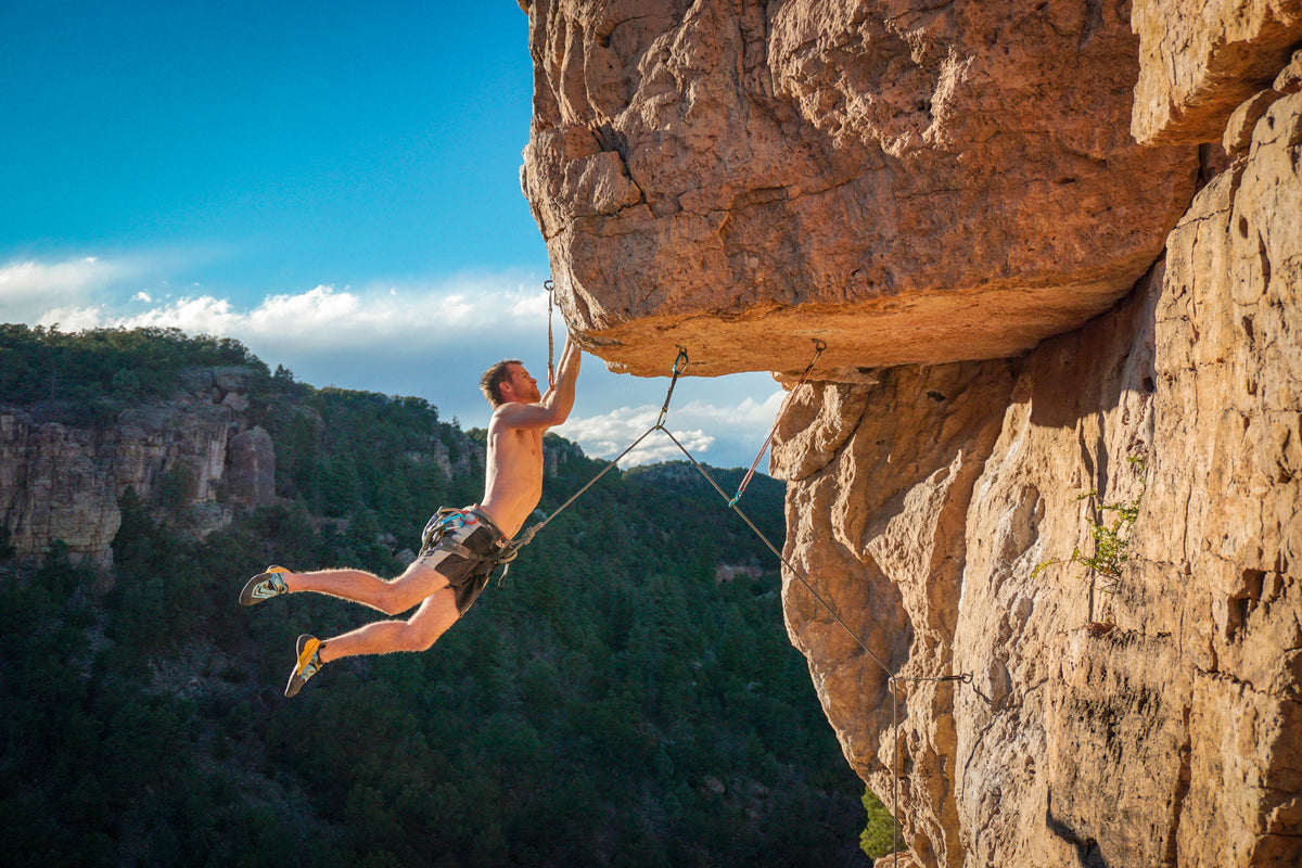harnessed person holds onto the edge of a rock cliff