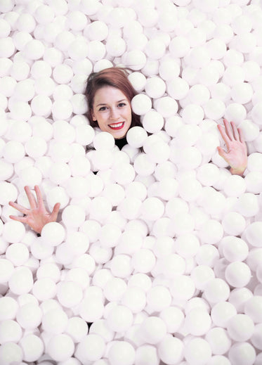 head and hands of a woman float in ball pit