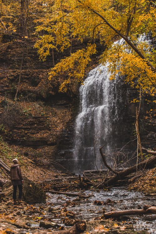 hiker looks up at waterfall in fall