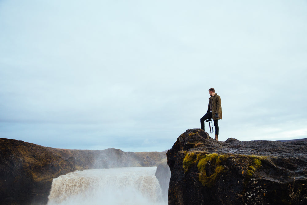 hiker on cliff by waterfall