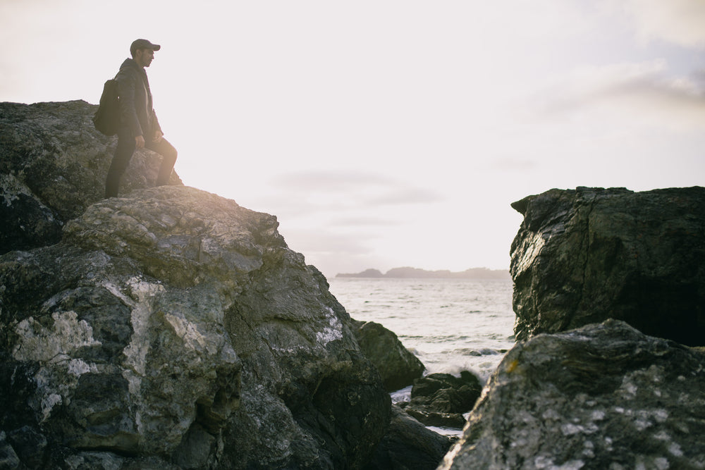 hiker stands on tall rock by ocean