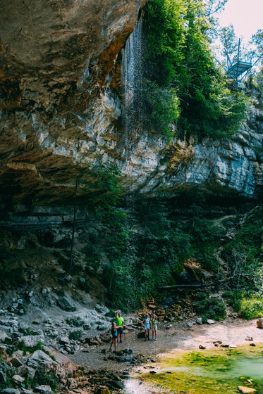 hikers under a rocky outcrop and small waterfall