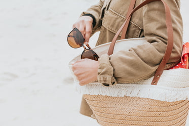 holding a beach bag and takes out their sunglasses