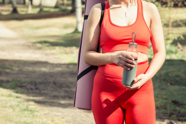 holding a yoga mat and water bottle in red workout gear