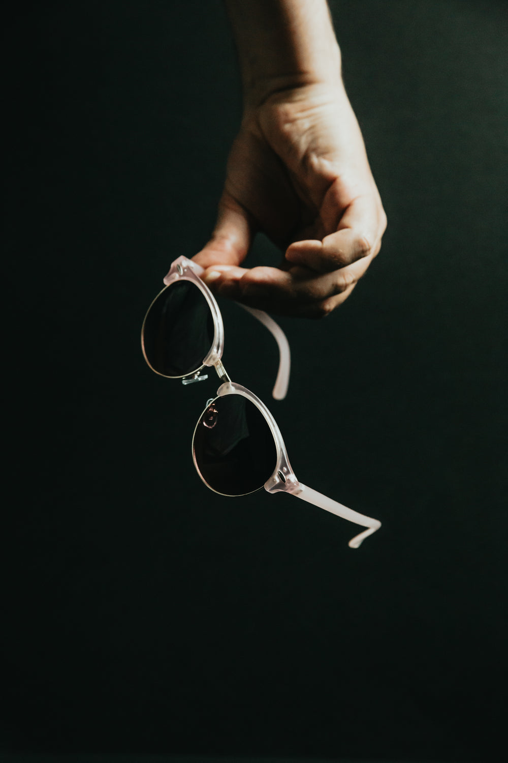 holding pink sunglasses against black background