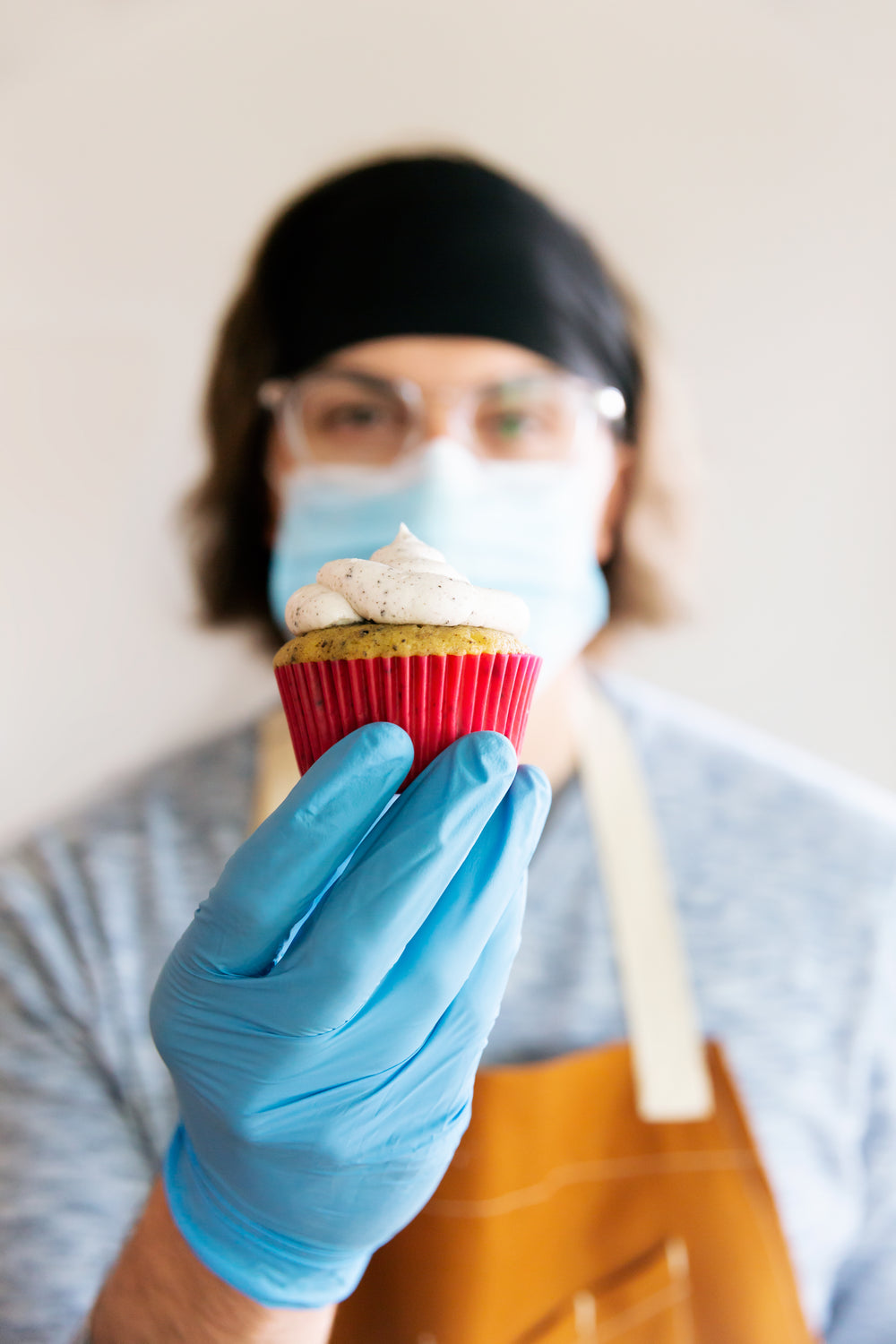 holding up a cupcake in gloves and mask