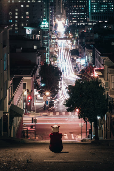 hooded figure sits on city street hill