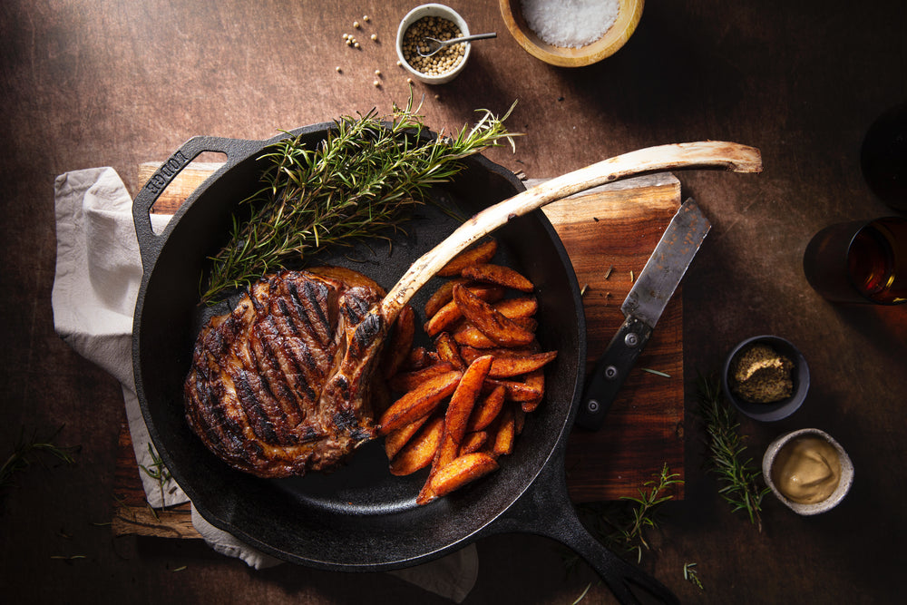 iron skillet with meat and potatoes on wooden board