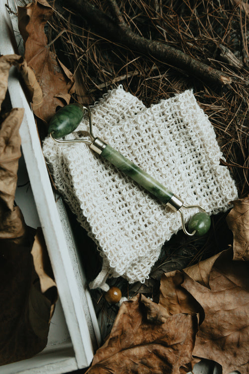 jade face roller flatlay surrounded by dried leaves