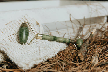 jade face roller lays on white cloth with pine needles