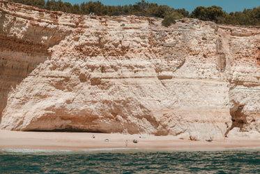 kayakers and surfers on a sandy beach under limestone cliffs