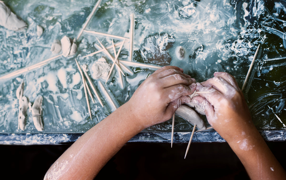 kids hands molding clay on a messy table top