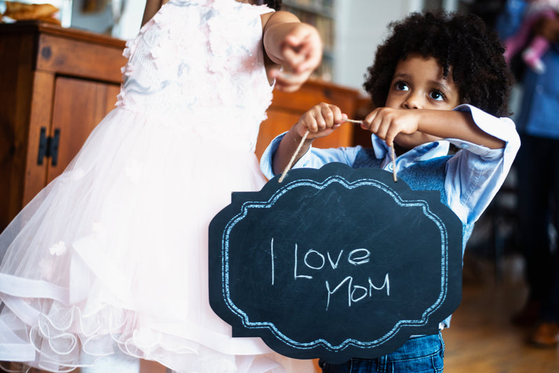 A young child holds up a chalkboard that says "I love Mom"