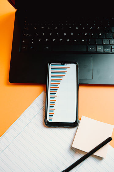 laptop and a cell phone showing a graph on orange table