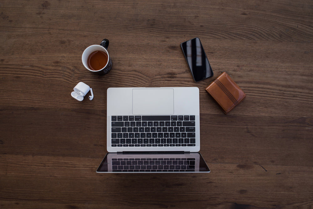 laptop with wallet, phone, earbuds, and tea