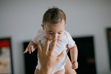 large hands hold a baby up and the baby looks down