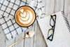 latte art on rustic table next to notebook and glasses