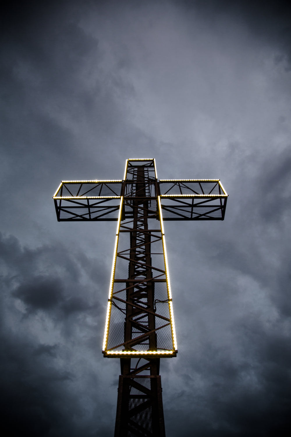 cruz iluminada a led diante de céu tempestuoso