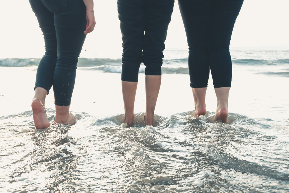 legs of three people walking into wavy water