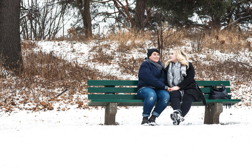 lesbian couple  holding hands on a green park bench