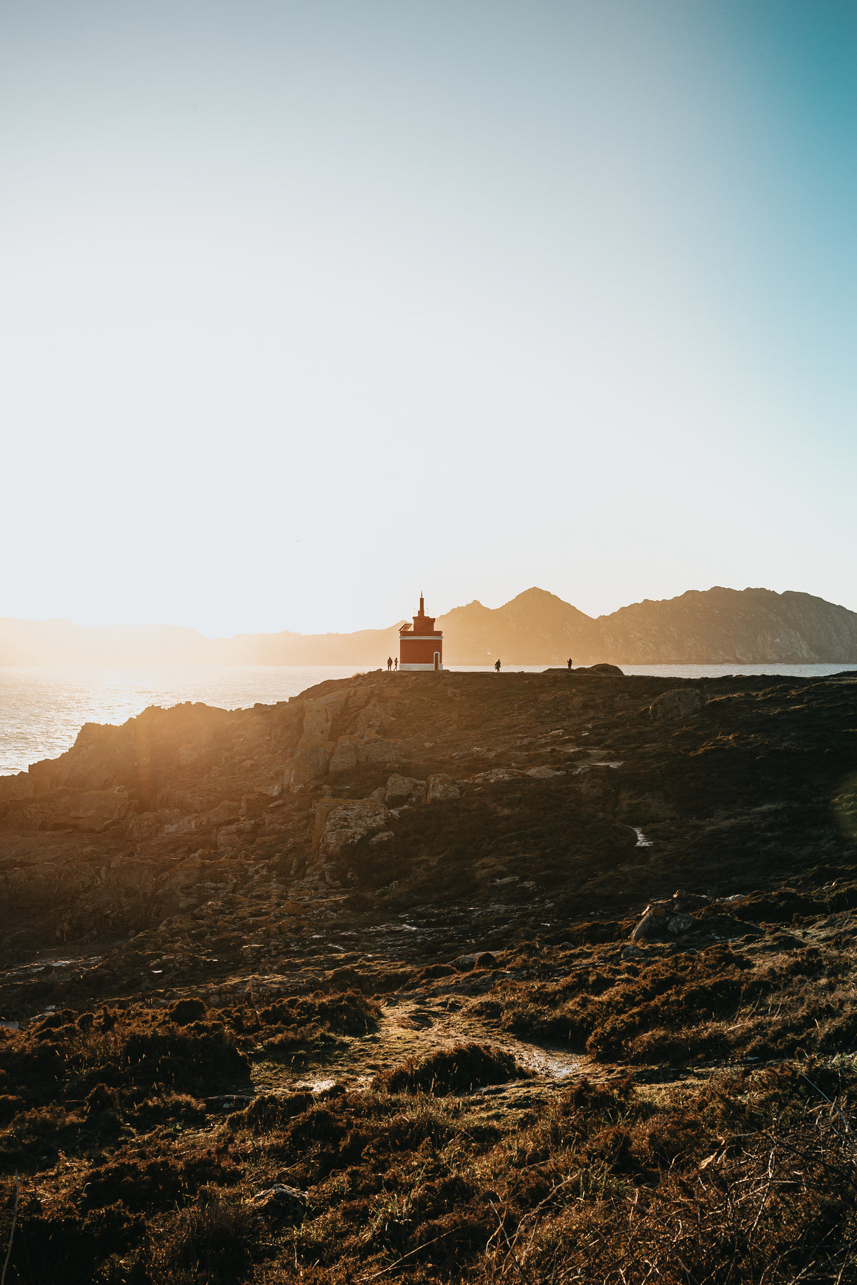lighthouse peaks over a cliff at sunset
