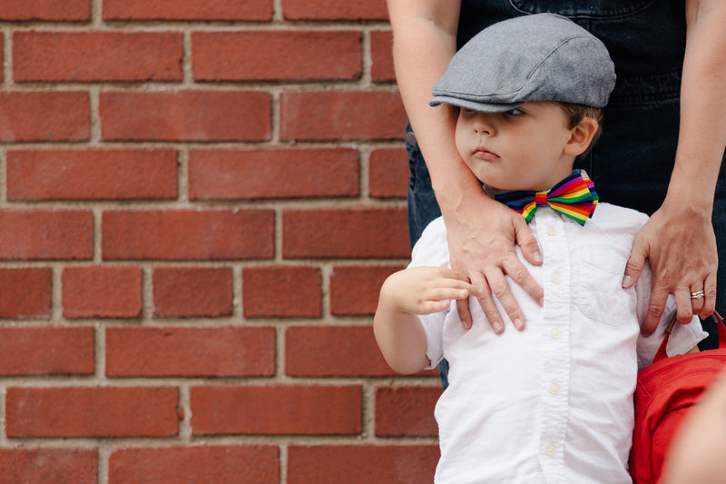Un bambino con un cappellino aspetta lo scuolabus. La madre tiene le mani sulle spalle del bambino per incoraggiarlo.