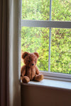 lone brown teddy bear sitting on window ledge