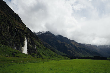 lush green fields by mountains and waterfall