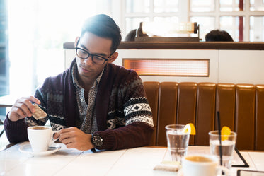 man adds sugar to coffee in cafe