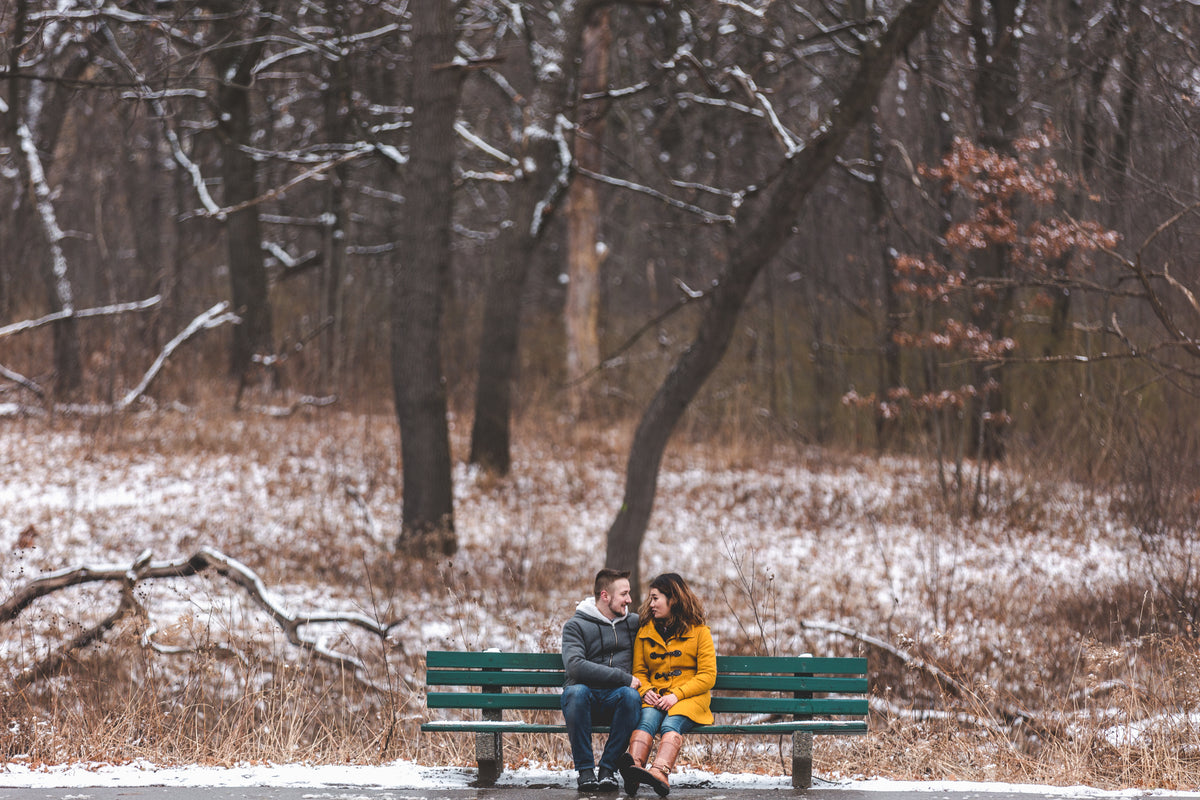 man and woman chat on a bench in a snowy park