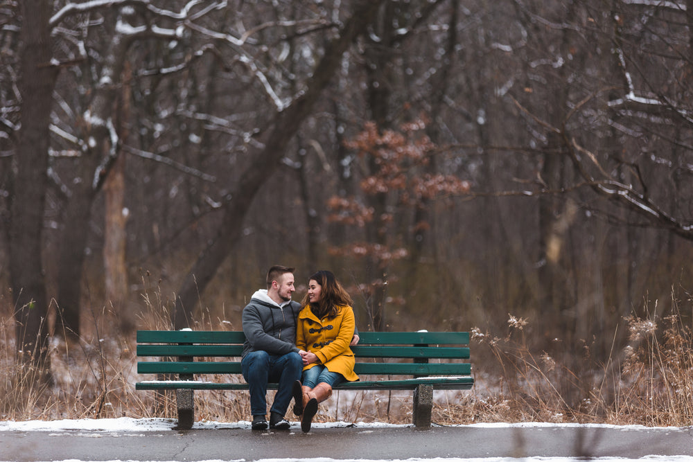 man and woman hold hands on a bench in a snowy park