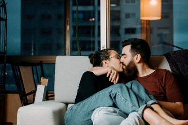 man and woman share a kiss sitting on grey couch indoors