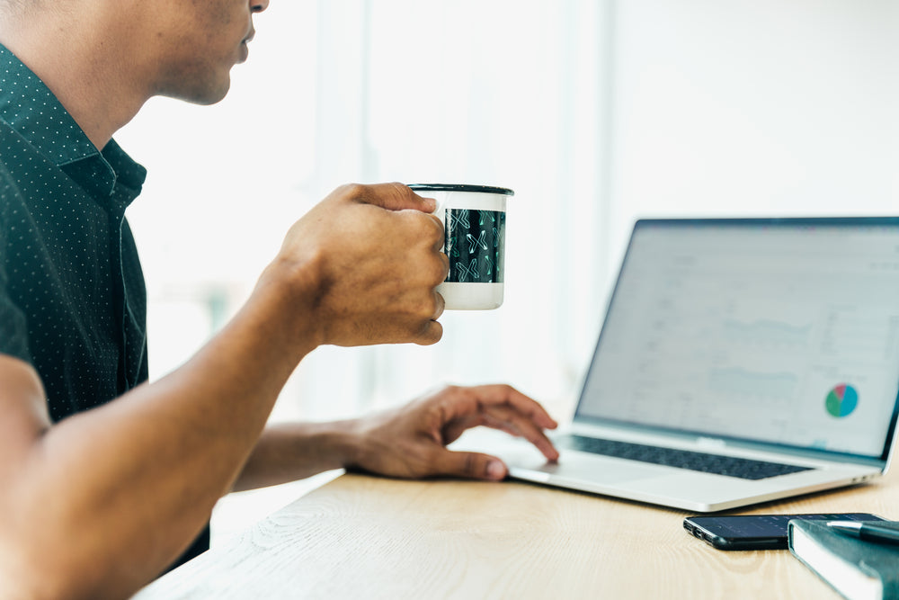 man at computer looking at graphs drinking coffee