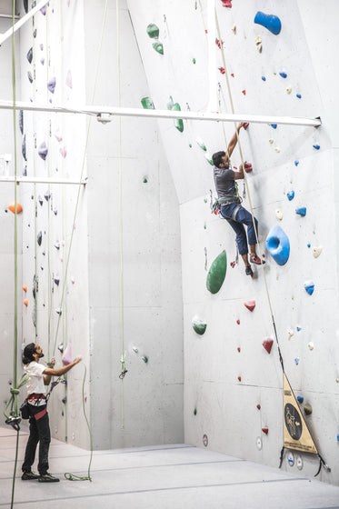 man bouldering with help from friend