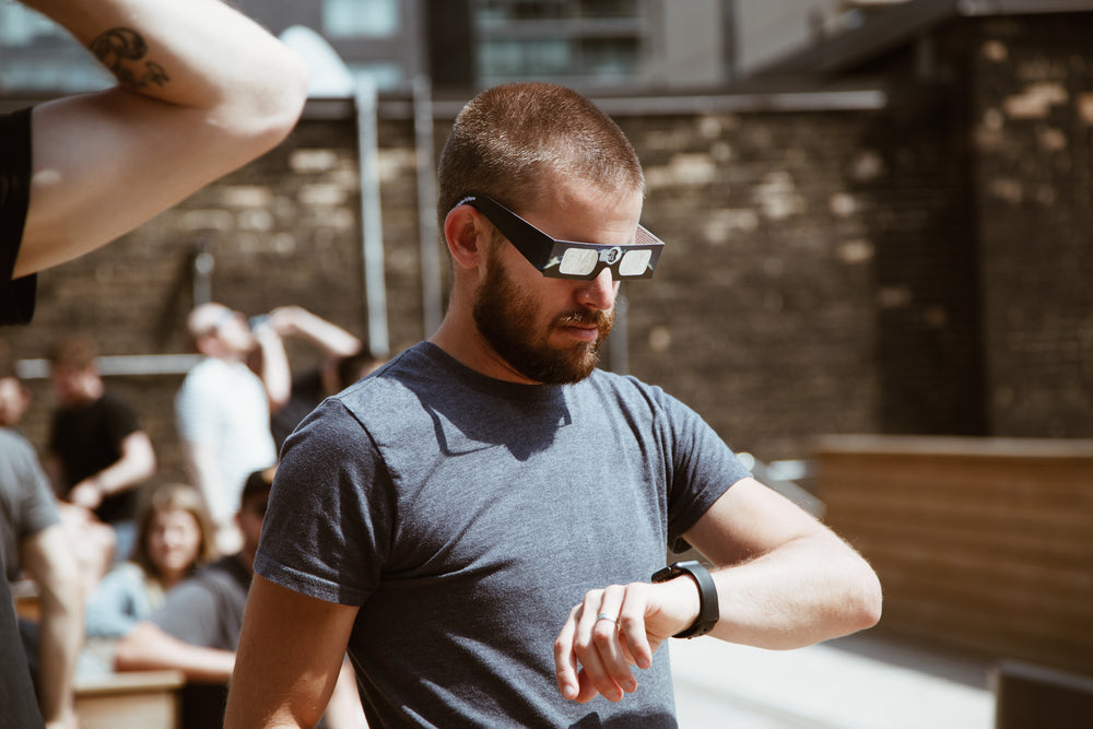 man checks time in eclipse glasses