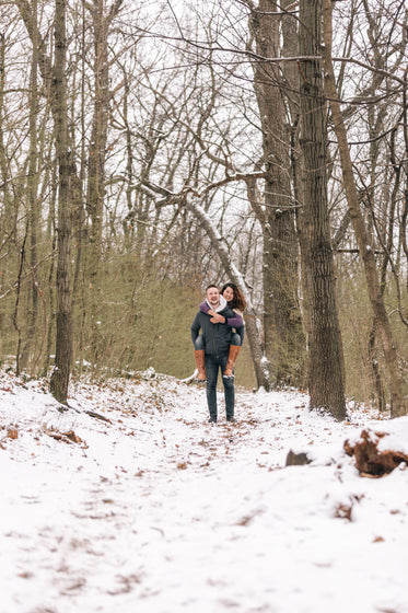 man gives woman a piggyback in the snowy woods