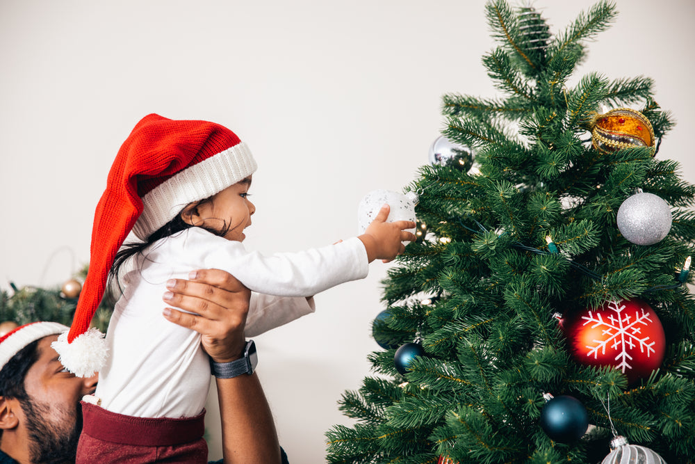 man helps toddler decorate christmas tree