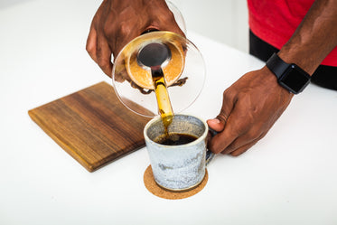 man holds cup and pours black coffee