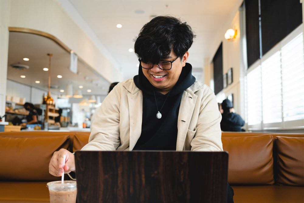 man in coffee shop sits in front on their laptop on a brown couch