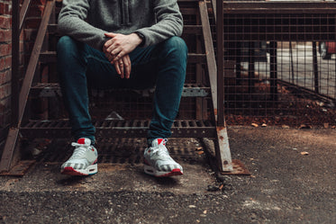 man in dark denim and fashion sneakers sitting on stairwell