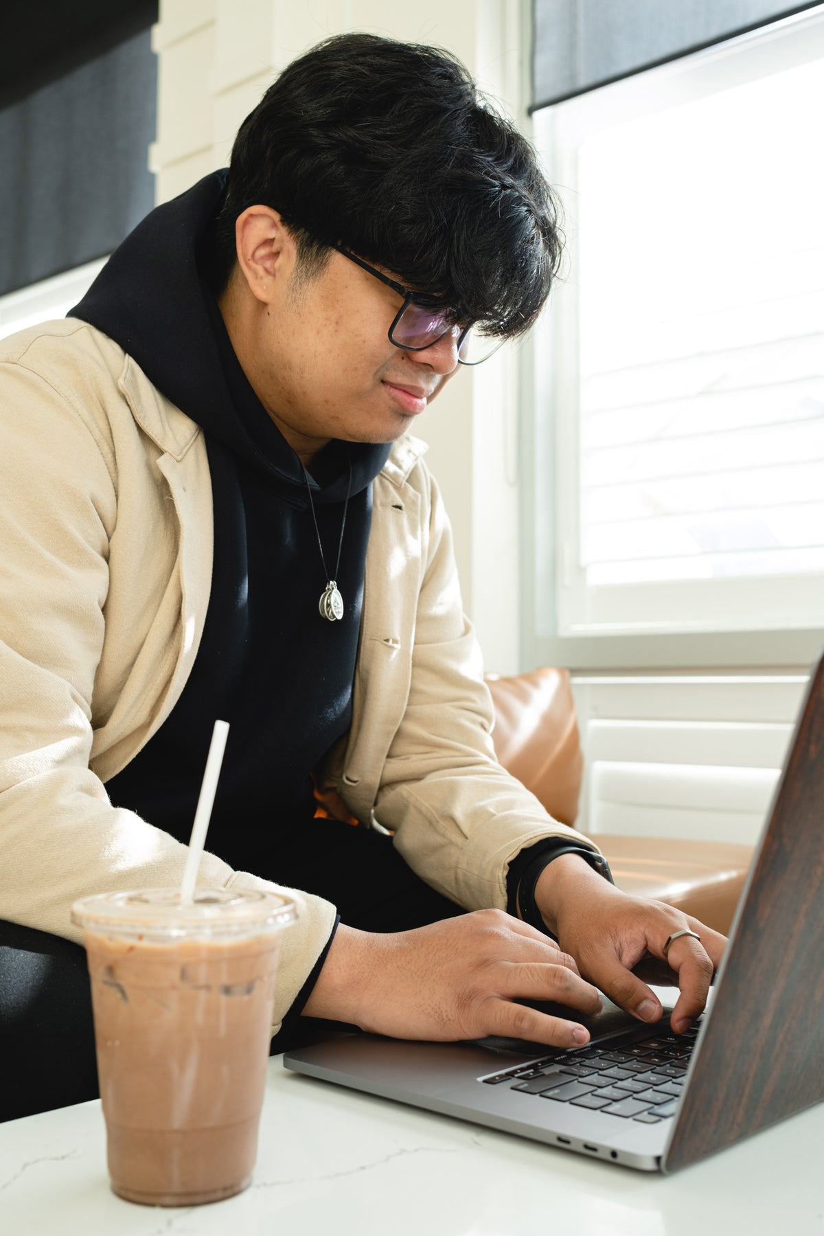 man in glasses types on a laptop beside iced coffee
