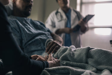 man in hospital bed comforted by friend as doctor looks on