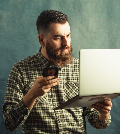man in plaid holds a laptop and cellphone