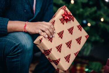 man kneels by christmas tree with present